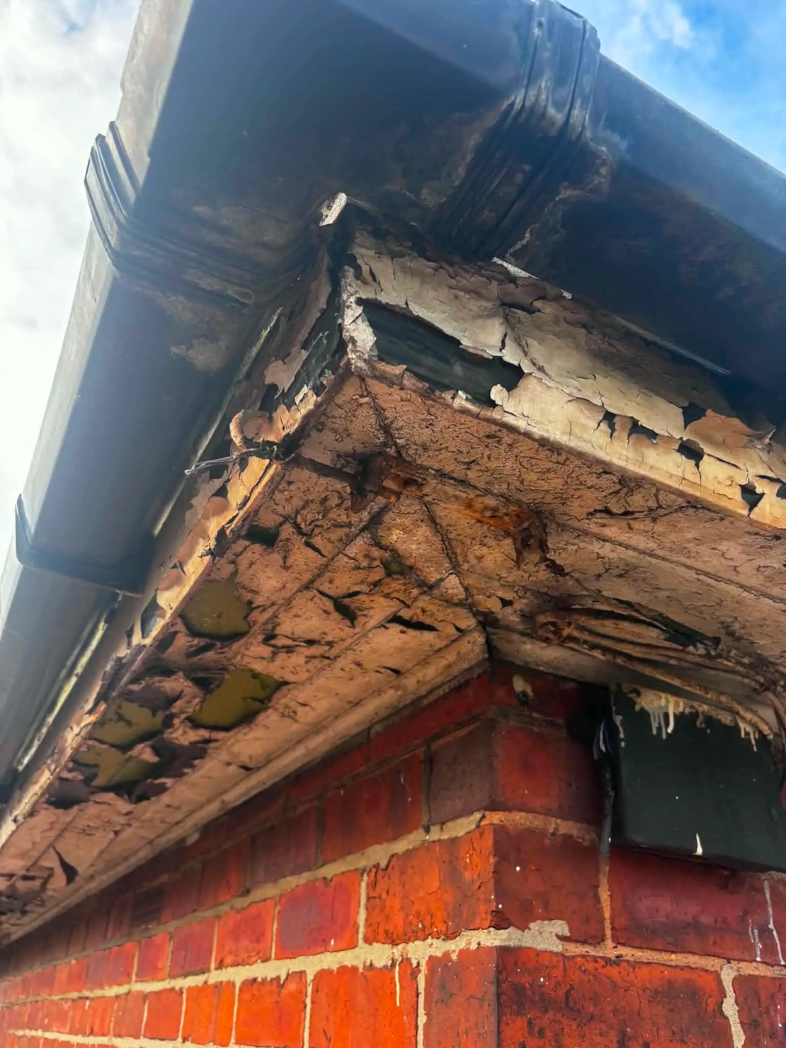 Severely rotten timber fascia and soffit at the corner of a brick property before replacement